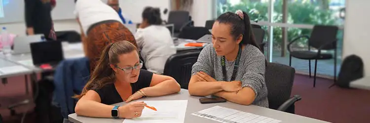 Teacher at a desk with a student working through a workbook.